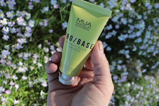 Close-up of a hand holding a makeup primer tube with flowers in the background, perfect for cosmetics brands.