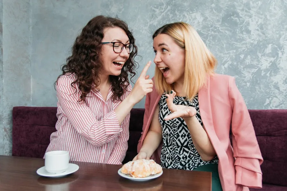Two young women enjoying a fun moment at a café, sharing laughter over coffee and pastries.