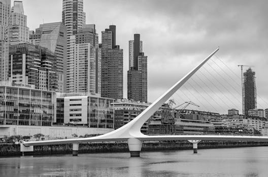 Black and white photo of iconic Puente de la Mujer bridge with Buenos Aires skyline in the background.