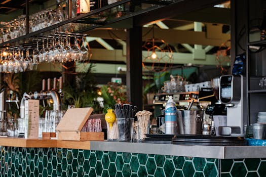 A modern cafe counter with hanging glassware, coffee machines, and bar tools, exuding vibrant cafe vibes.
